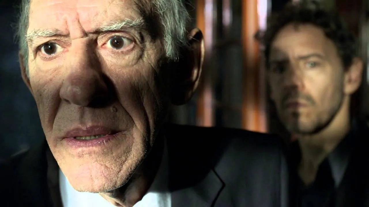 Still from Psi: an elderly man stares into the camera, troubled, while the analyst watches from behind him.