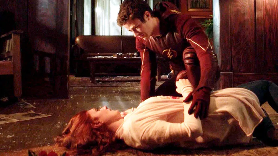 Barry, in the Flash suit, kneels over his dying mother on the living-room floor.
