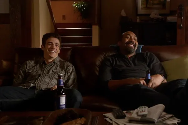 Barry and his foster father, Joe West, laughing together on the couch with beers.