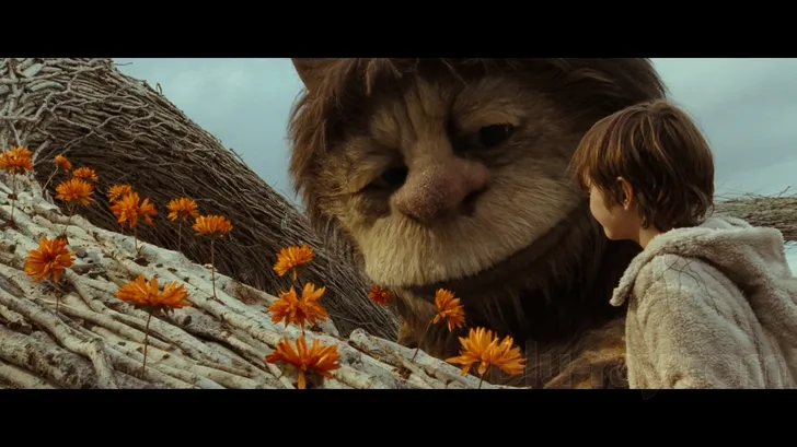 Still from Where the Wild Things Are: Max faces one of the huge, shaggy Wild Things across a row of orange flowers.